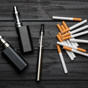 Cigarettes and different vaping devices on black wooden background, flat lay. Smoking alternative